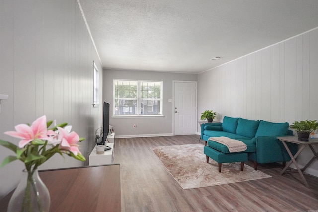 living room featuring visible vents, ornamental molding, a textured ceiling, wood finished floors, and baseboards