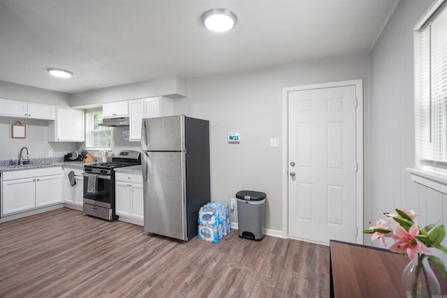 kitchen featuring white cabinets, wood finished floors, light stone countertops, stainless steel appliances, and under cabinet range hood