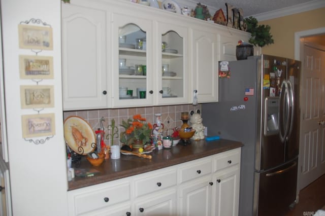 kitchen featuring white cabinetry, ornamental molding, tasteful backsplash, stainless steel fridge, and glass insert cabinets