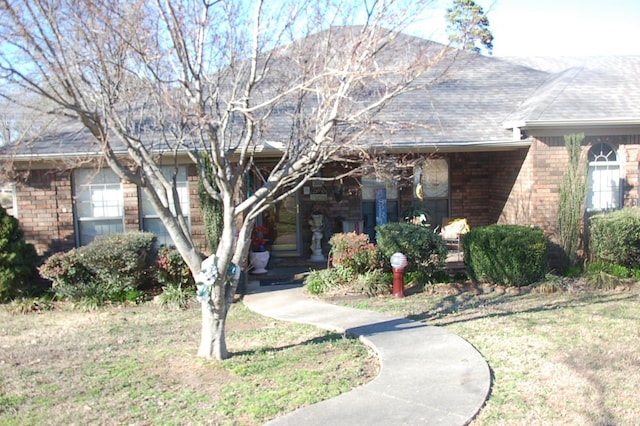 ranch-style house featuring a front yard, covered porch, brick siding, and roof with shingles