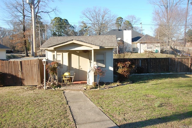 view of front of house with a shingled roof, fence, an outbuilding, and a front yard