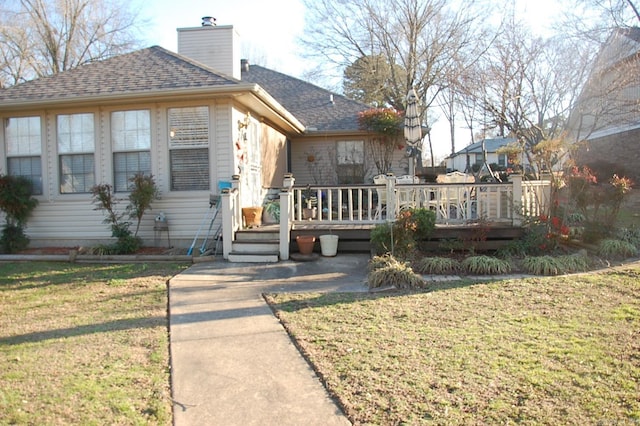 view of front facade featuring a wooden deck, a chimney, roof with shingles, and a front yard