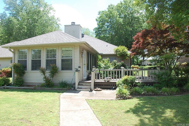 view of front of house featuring a deck, a chimney, a shingled roof, and a front lawn