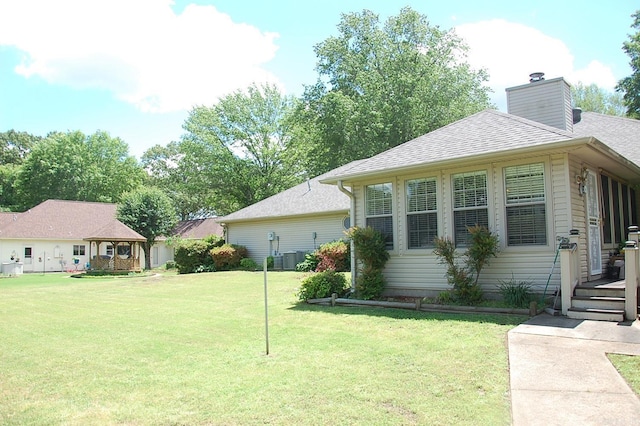 view of side of home with a gazebo, a lawn, roof with shingles, and a chimney