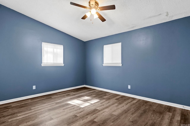 spare room with a textured ceiling, wood finished floors, a ceiling fan, baseboards, and vaulted ceiling