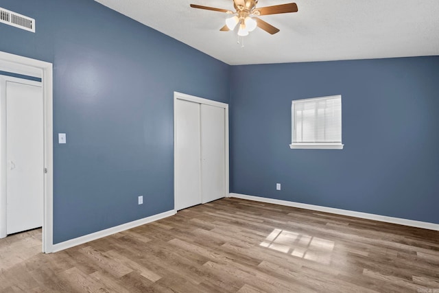 unfurnished bedroom featuring baseboards, visible vents, a ceiling fan, wood finished floors, and a closet