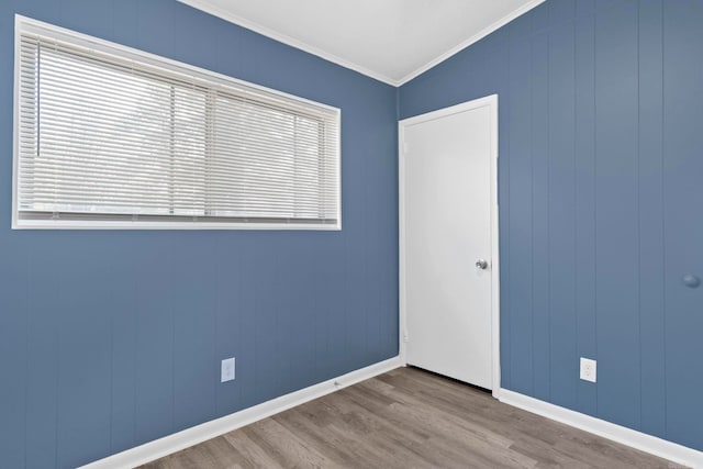 spare room featuring crown molding, baseboards, and wood finished floors