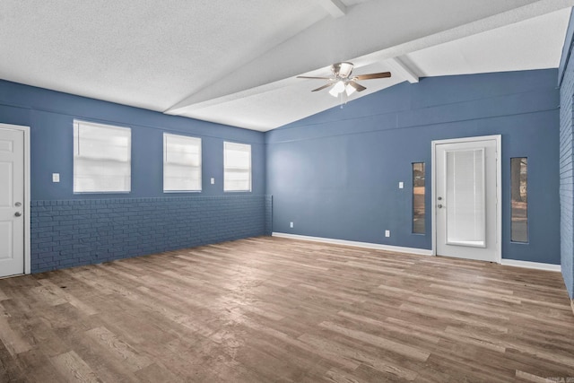 empty room with a ceiling fan, vaulted ceiling with beams, brick wall, and wood finished floors