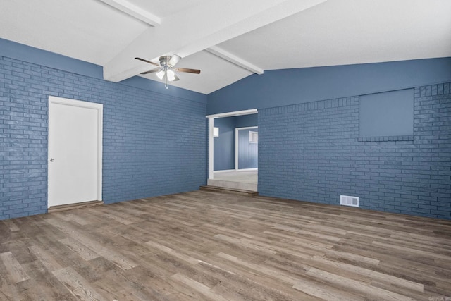 unfurnished room featuring ceiling fan, brick wall, wood finished floors, and visible vents