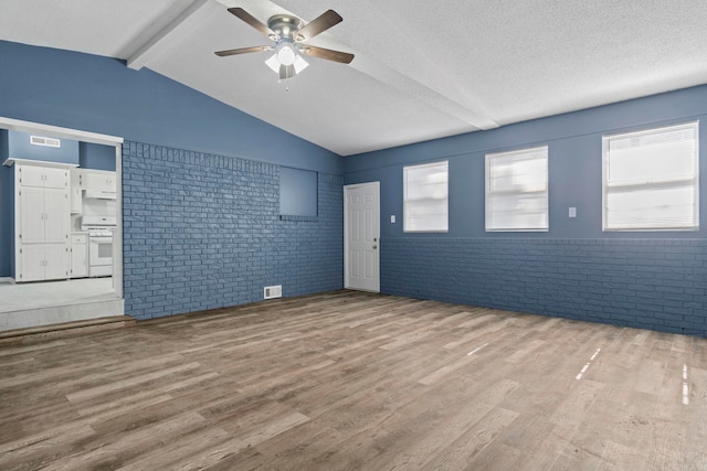 empty room featuring a textured ceiling, brick wall, wood finished floors, and visible vents