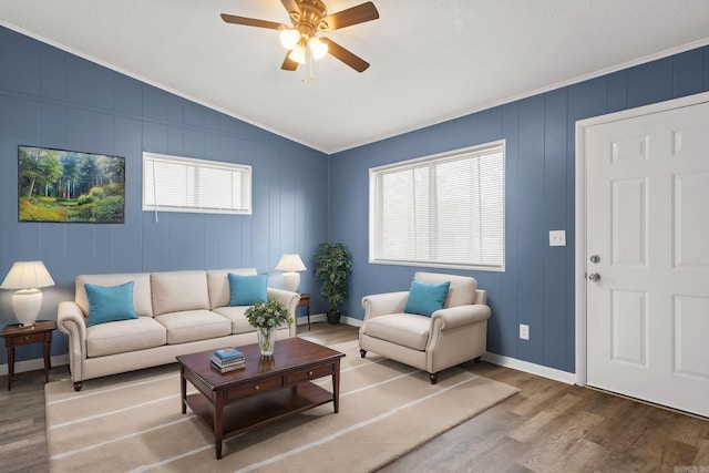 living area with lofted ceiling, ceiling fan, wood finished floors, baseboards, and crown molding