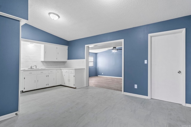 kitchen featuring lofted ceiling, light countertops, a ceiling fan, white cabinetry, and a textured ceiling