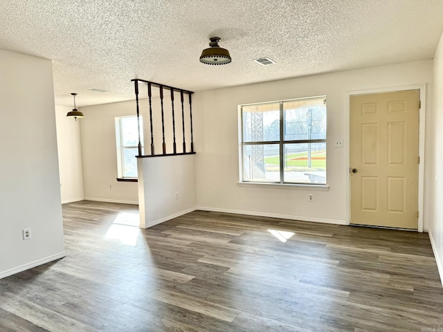 interior space with a textured ceiling, dark wood-type flooring, visible vents, and baseboards