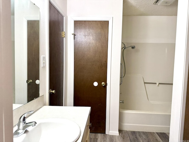 bathroom featuring a textured ceiling, tub / shower combination, wood finished floors, and vanity