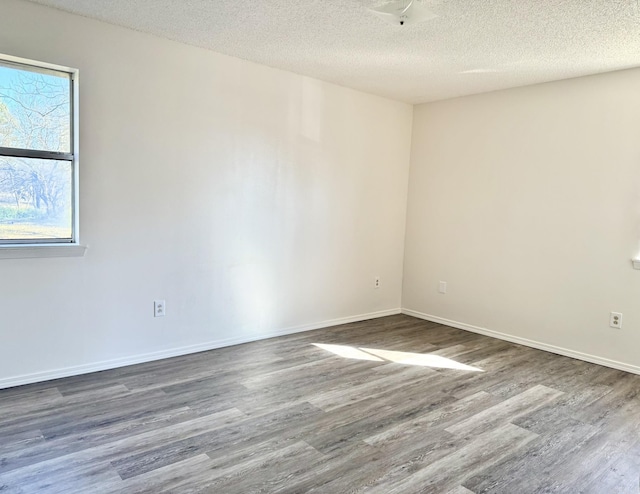 empty room with a textured ceiling, baseboards, and wood finished floors