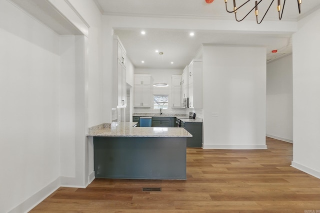 kitchen with appliances with stainless steel finishes, white cabinets, a peninsula, and light wood finished floors