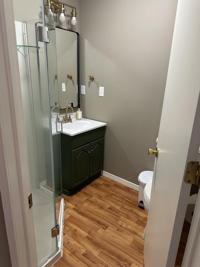 bathroom with baseboards, toilet, wood finished floors, vanity, and a shower stall