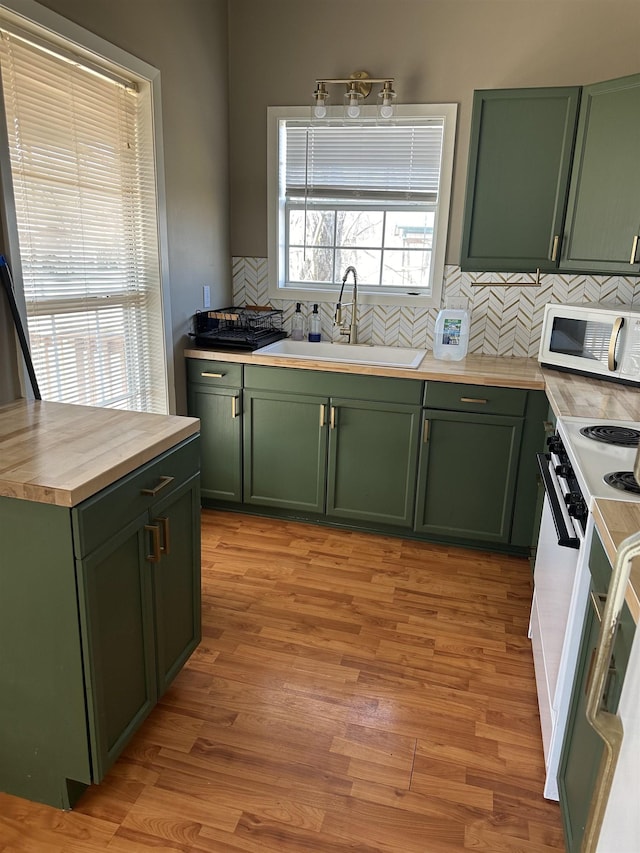 kitchen with range with electric stovetop, green cabinets, white microwave, a sink, and wood counters