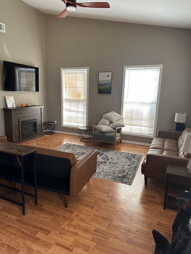 living area featuring light wood-style floors, a glass covered fireplace, visible vents, and a ceiling fan