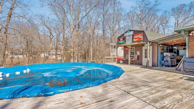 view of swimming pool with a grill, a wooden deck, and an outdoor structure