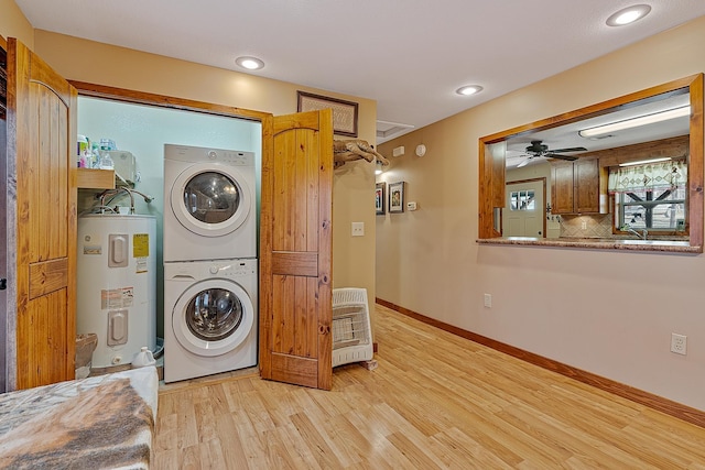 laundry area with electric water heater, laundry area, baseboards, light wood-style floors, and stacked washing maching and dryer