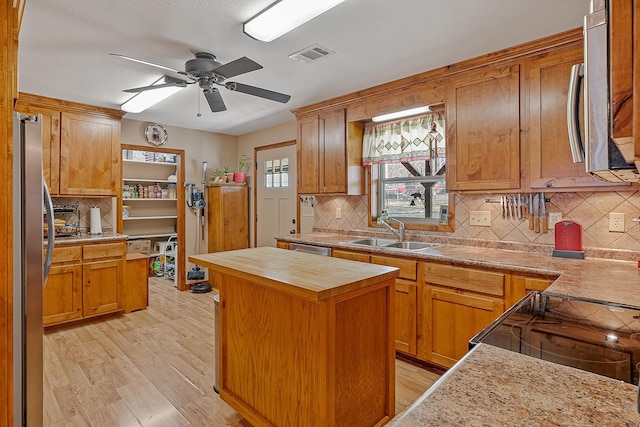 kitchen with stainless steel appliances, a sink, visible vents, light wood-type flooring, and a center island