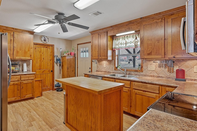 kitchen featuring visible vents, a center island, stainless steel appliances, light wood-type flooring, and a sink