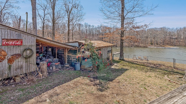 view of yard with a wooded view, a water view, fence, and an outdoor structure