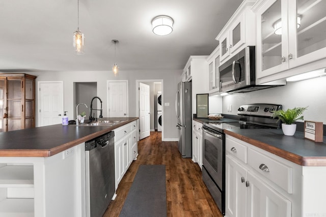 kitchen featuring appliances with stainless steel finishes, dark countertops, stacked washer / drying machine, and a sink