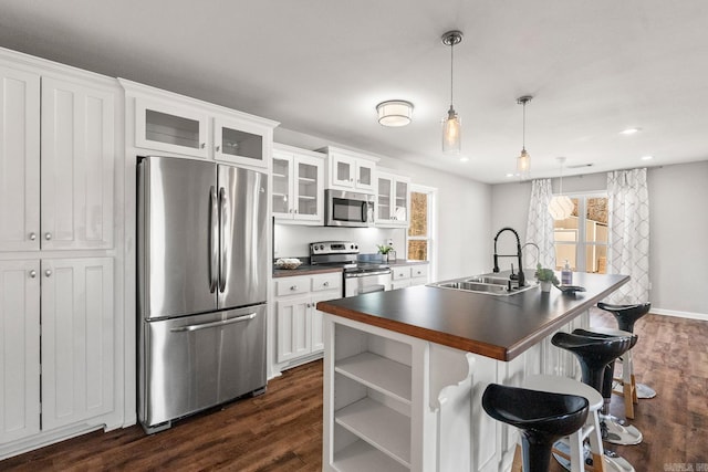 kitchen with white cabinets, dark countertops, dark wood-style flooring, stainless steel appliances, and a sink