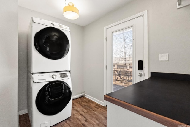 washroom featuring stacked washing maching and dryer, baseboards, laundry area, and dark wood-type flooring