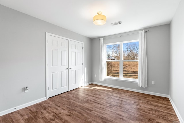 unfurnished bedroom featuring a closet, wood finished floors, visible vents, and baseboards