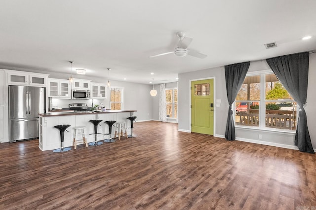 kitchen featuring dark wood-style flooring, visible vents, appliances with stainless steel finishes, white cabinetry, and an island with sink