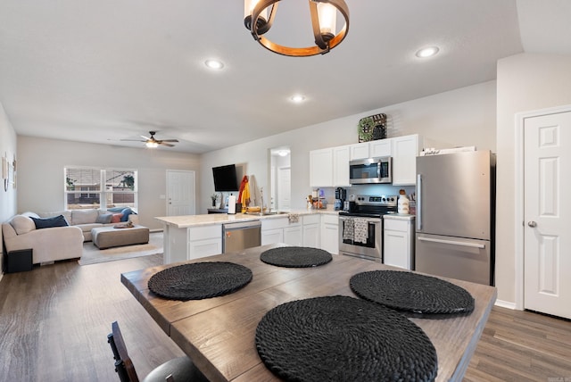 kitchen with appliances with stainless steel finishes, wood finished floors, a peninsula, light countertops, and white cabinetry