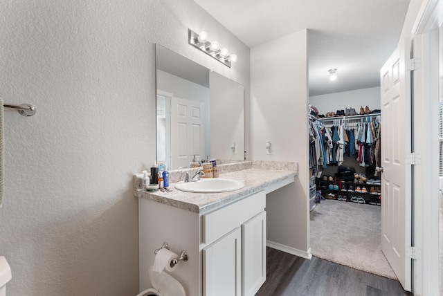 bathroom with a walk in closet, a textured wall, vanity, and wood finished floors