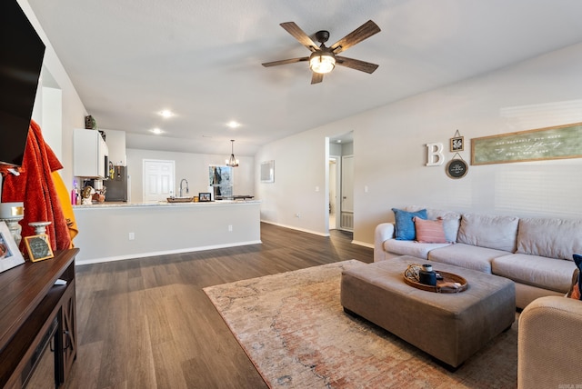 living room featuring ceiling fan with notable chandelier, dark wood finished floors, and baseboards