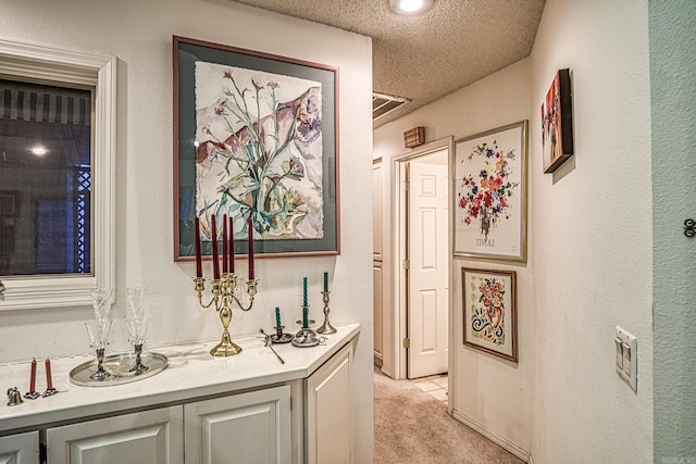 corridor with a textured ceiling, a textured wall, and light colored carpet