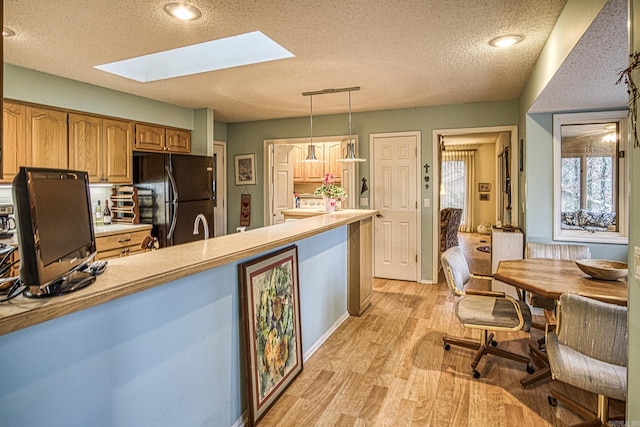 kitchen with a skylight, light wood-style flooring, decorative light fixtures, freestanding refrigerator, and light countertops