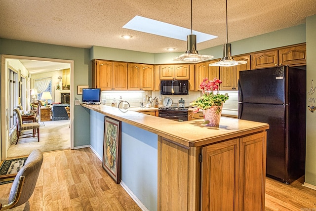 kitchen with a skylight, a peninsula, light countertops, light wood-type flooring, and black appliances