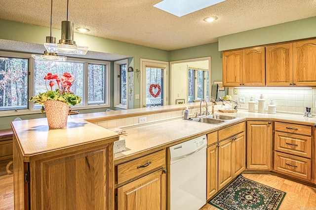 kitchen featuring a skylight, light wood-style flooring, a sink, dishwasher, and a peninsula