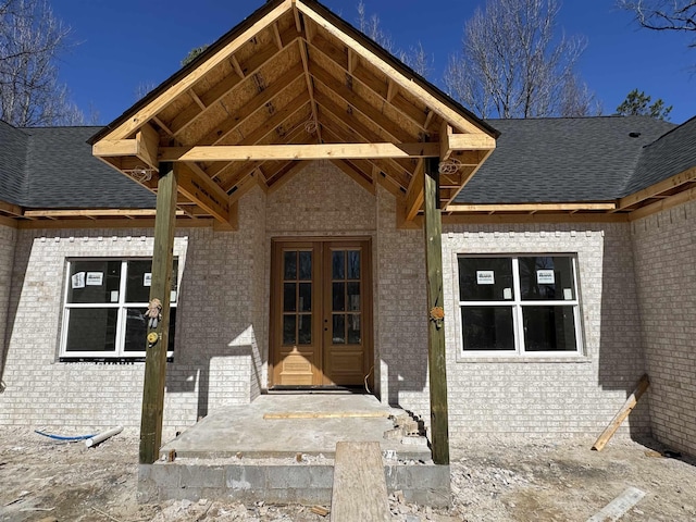 property entrance featuring a shingled roof, french doors, and brick siding