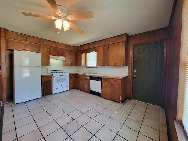 kitchen with light countertops, brown cabinetry, a sink, white appliances, and under cabinet range hood