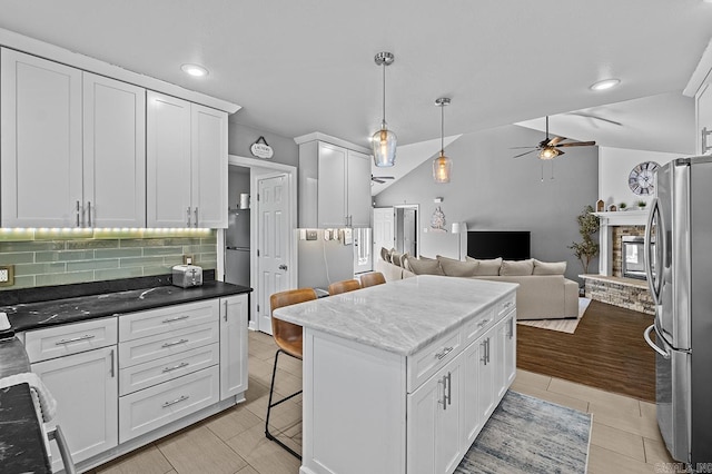 kitchen with freestanding refrigerator, open floor plan, white cabinetry, vaulted ceiling, and a stone fireplace