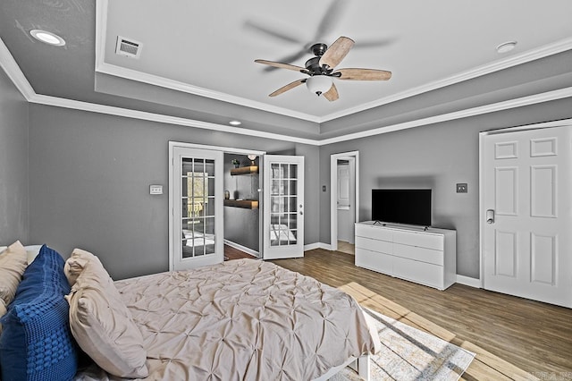 bedroom with crown molding, visible vents, a raised ceiling, and wood finished floors