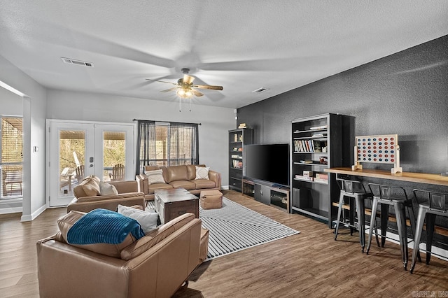 living area featuring french doors, visible vents, a textured wall, and wood finished floors