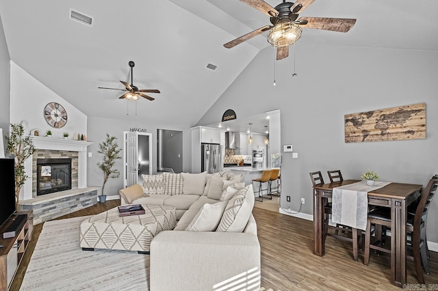 living room featuring a stone fireplace, visible vents, and light wood-style floors