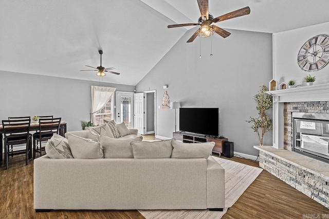 living room featuring ceiling fan, high vaulted ceiling, a fireplace, wood finished floors, and baseboards