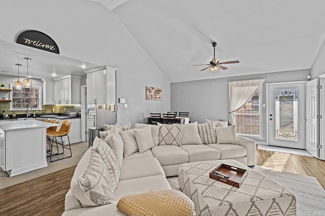 living area with high vaulted ceiling, light wood-style floors, a ceiling fan, and a wealth of natural light