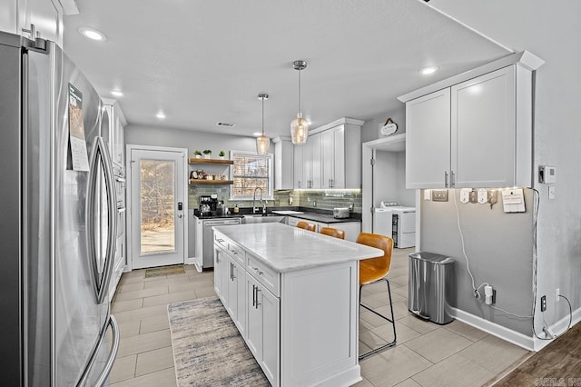 kitchen featuring open shelves, stainless steel appliances, decorative backsplash, washer and dryer, and a kitchen bar