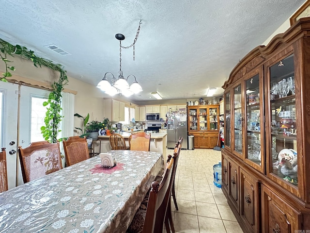 dining area featuring light tile patterned floors, a textured ceiling, visible vents, and an inviting chandelier